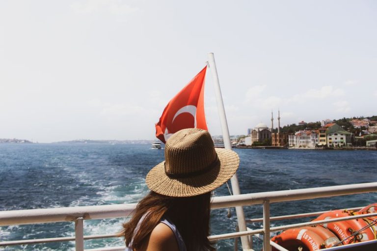 A woman in a straw hat enjoys a boat ride, with a view of Istanbul landmarks and the Turkish flag.