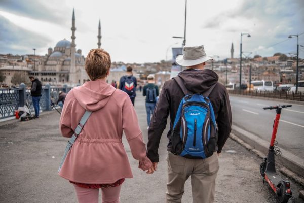 A couple walks hand in hand on a bridge in Istanbul with a mosque in the background.