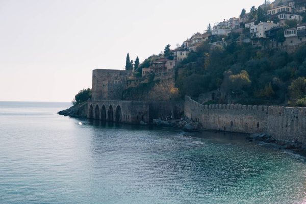 Scenic view of Alanya Castle with serene seashore and hillside dwellings in Turkey.