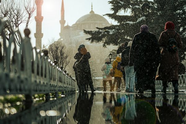 People walking in the snow near a mosque